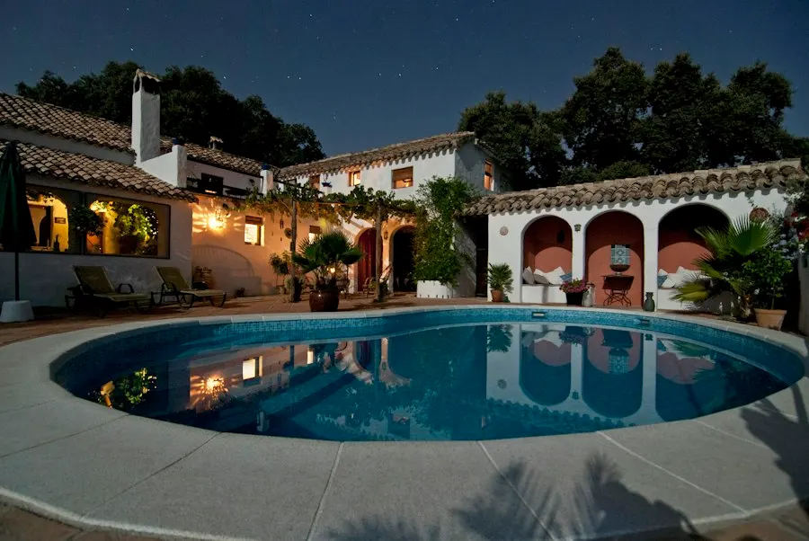 Courtyard home with arched alcoves and a tile roof around an oval pool, lit at night