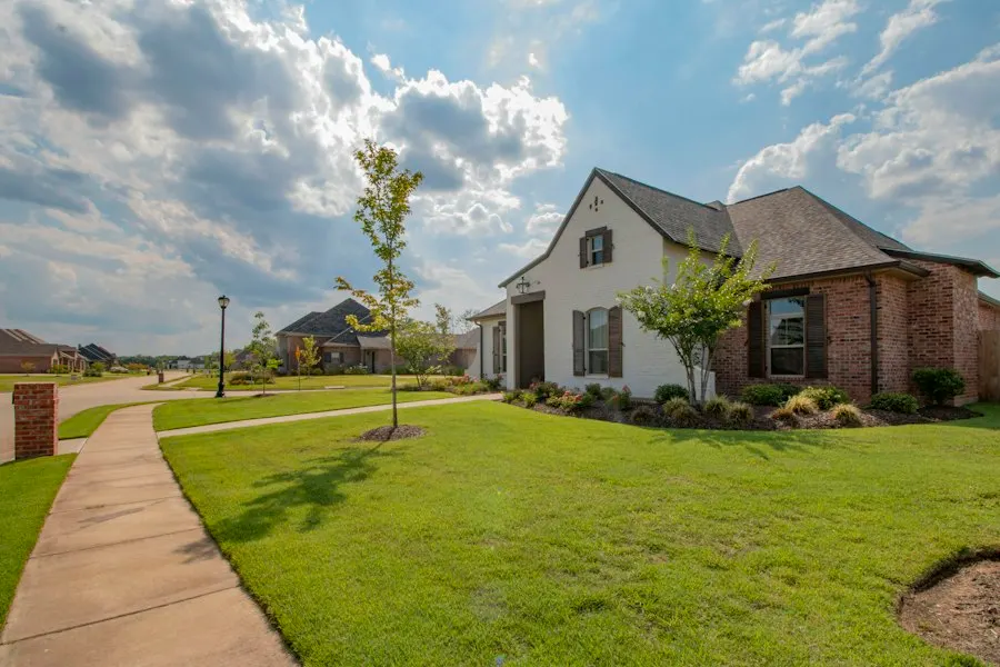 Brick and white-painted house with a green lawn and a tree-lined sidewalk in a suburban neighborhood