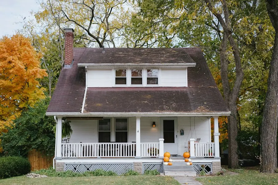 White two-story bungalow with a covered front porch surrounded by autumn trees