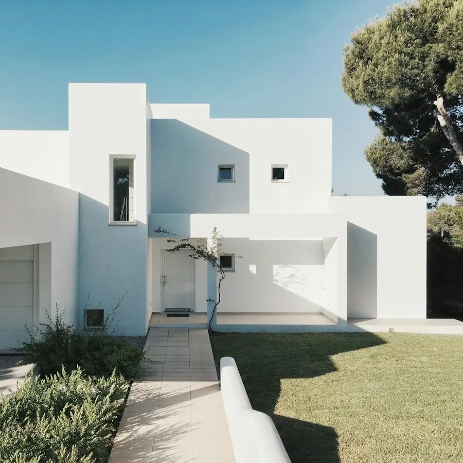 Modern white home with a flat roof and tall narrow windows beside a lawn and pine tree
