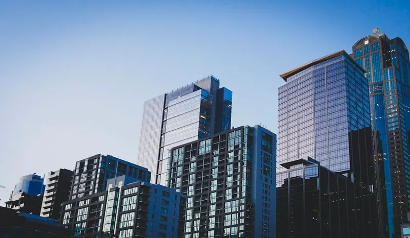 Cluster of glass and concrete high-rise buildings of different heights seen from street level against a clear blue sky