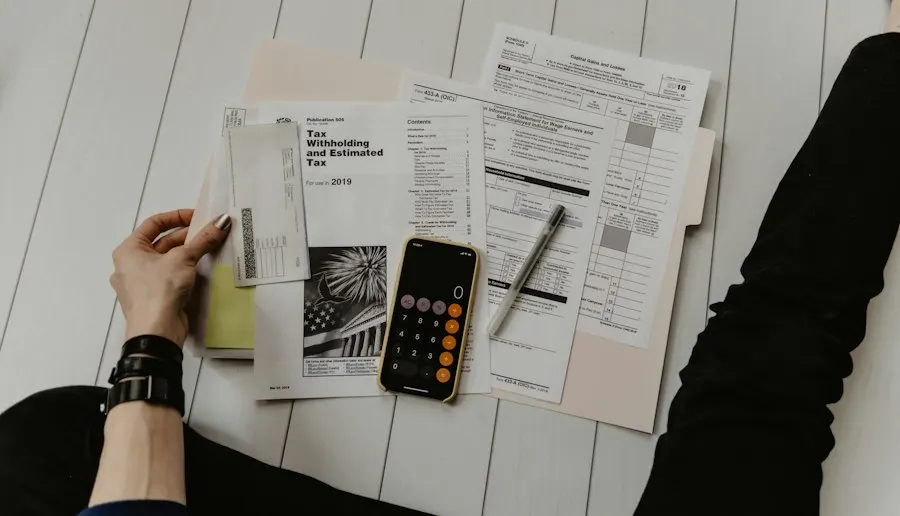 Hands holding tax forms and envelopes spread on a white floor beside a phone calculator and a pen